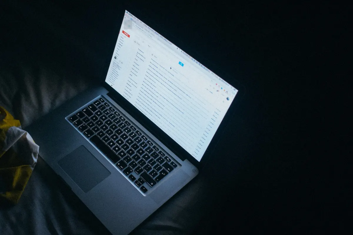 Ordinateur portable allumé dans la pénombre, l’écran affiche une boîte de réception d’e-mails