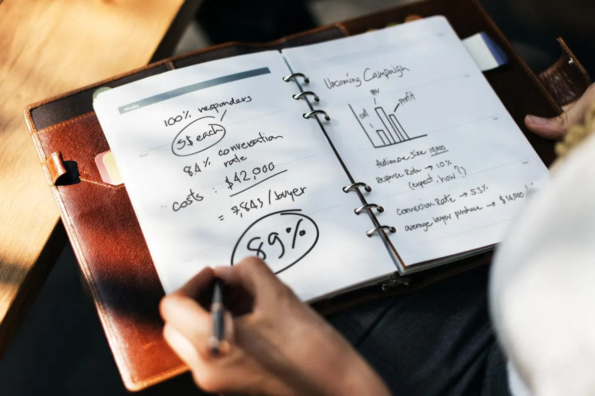 Carnet ouvert sur un plan de campagne marketing annoté à la main : objectifs, coûts, taux de conversion